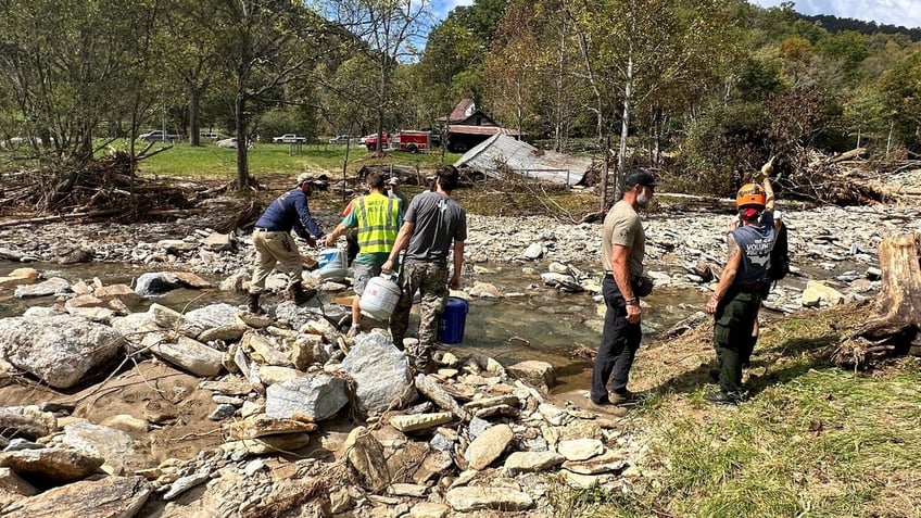 Volunteers cross a creek to deliver supplies in North Carolina after Hurricane Helene