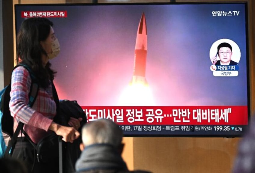 People watch a television screen showing a news broadcast with file footage of a North Kor