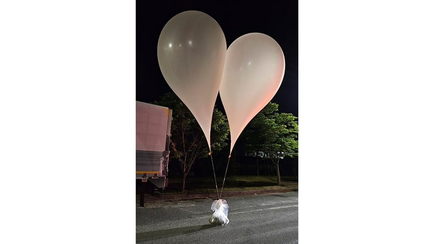 Large white balloons are tied to a plastic bag full of trash.