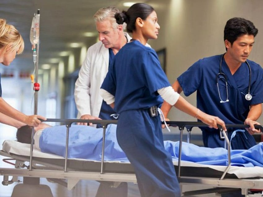 Doctor and nurses wheeling patient in gurney through hospital corridor - stock photo