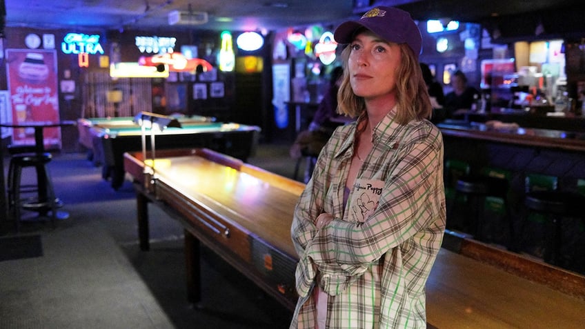 India Oxenberg wearing a plaid shirt and a hat inside a bar