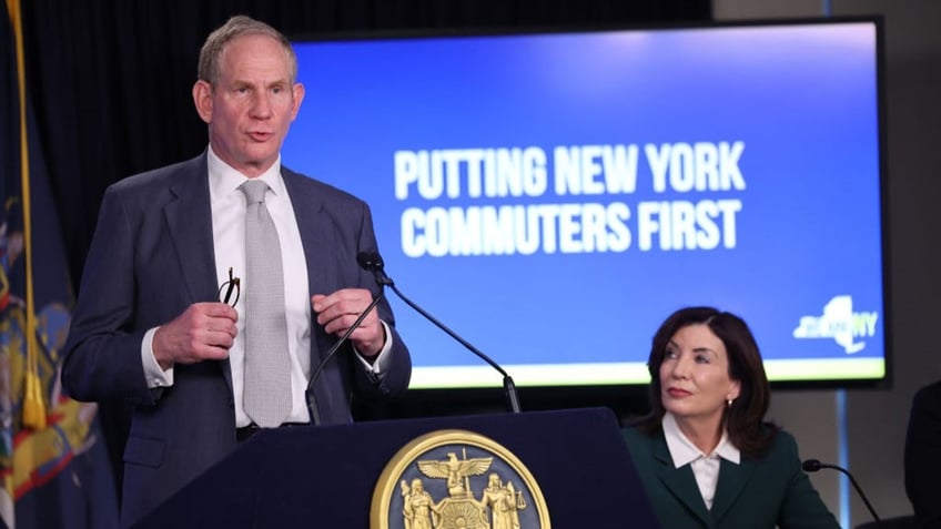 Janno Lieber, standing, with Gov. Hochul seated at right