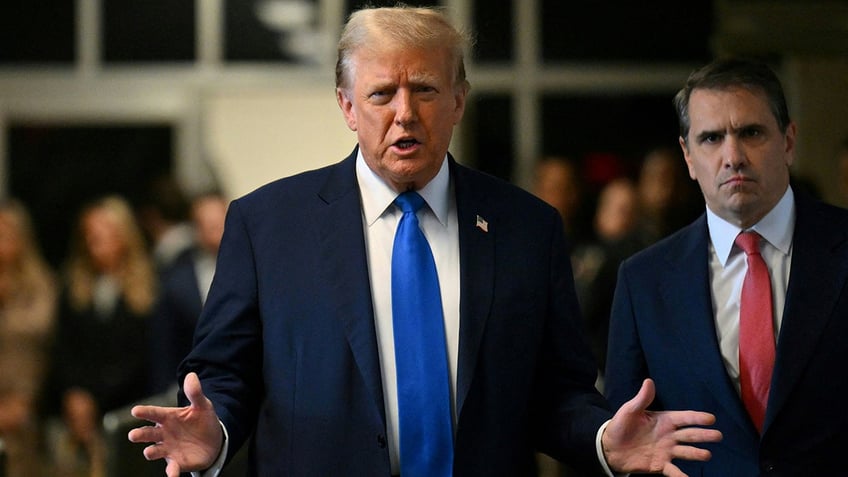 in blue tie, gesturing while talking to media