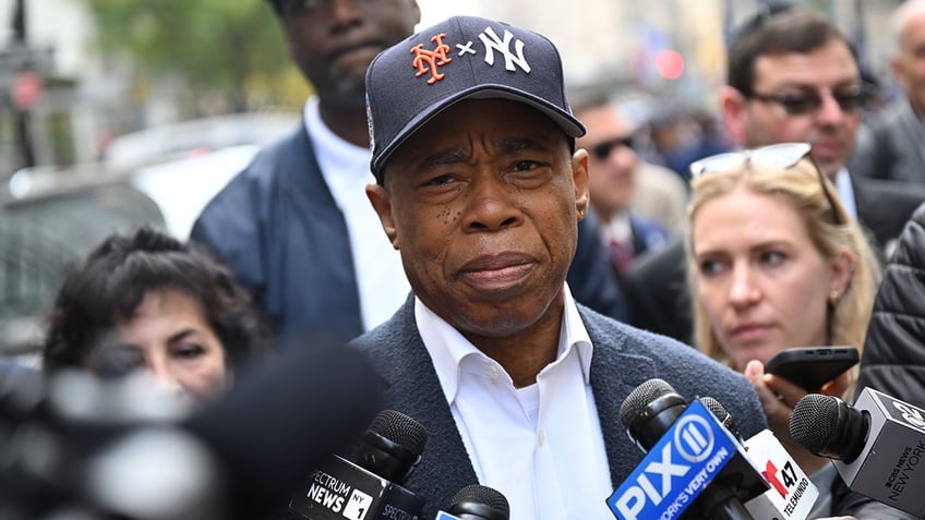 Eric Adams in middle of press gaggle with ball cap on