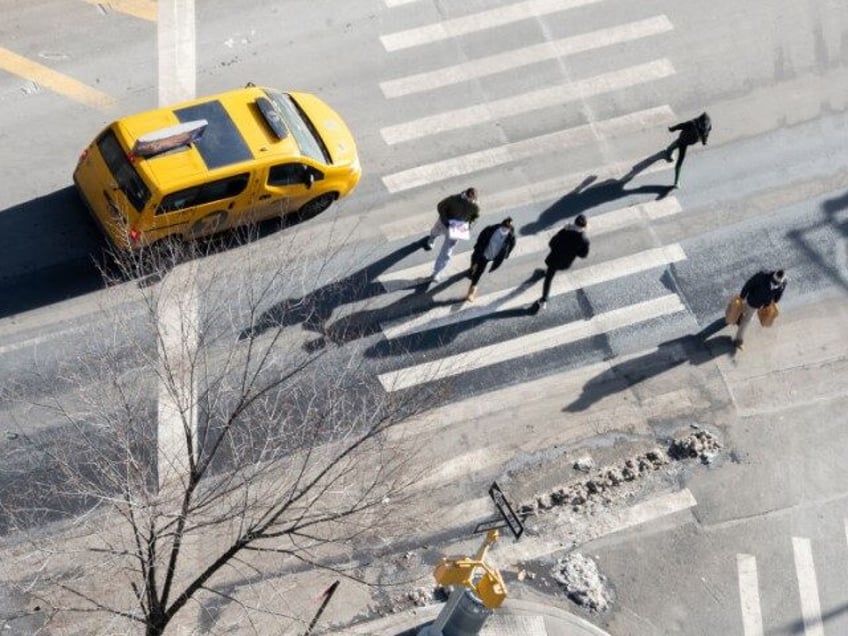 An aerial view of people casting shadows while walking across the street in front of a NYC