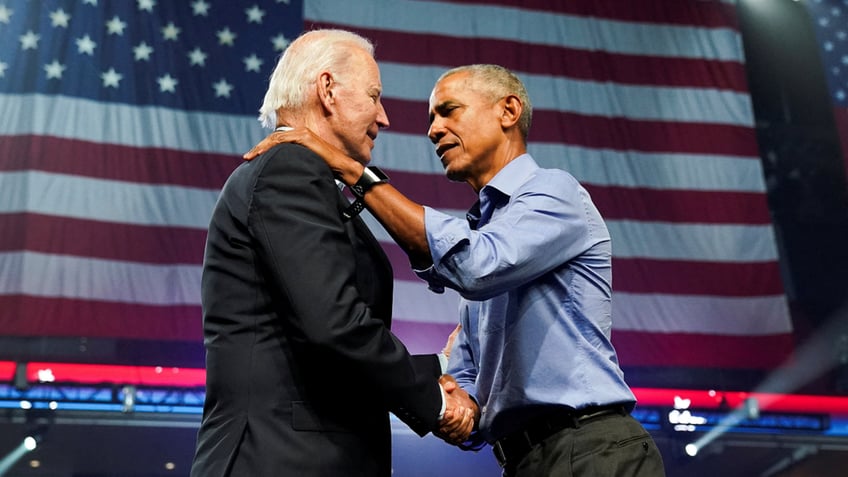Barack Obama with arms on Biden's shoulders, large US flag hanging in background