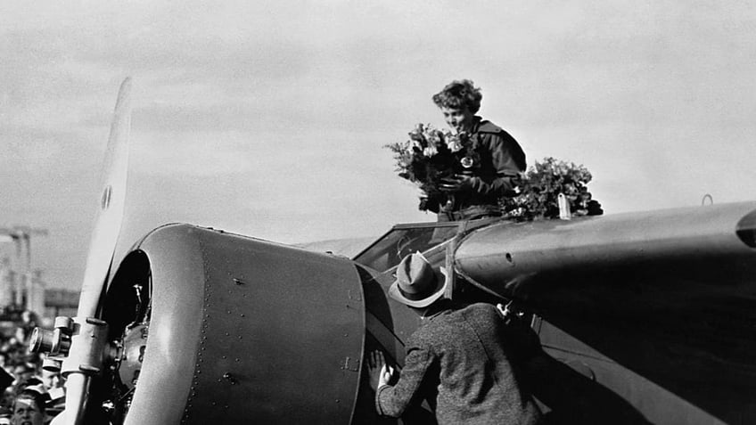 Amelia Earhart holding flowers on her plane