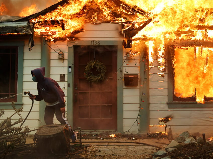 A person uses a garden hose in an effort to save a neighboring home from catching fire dur