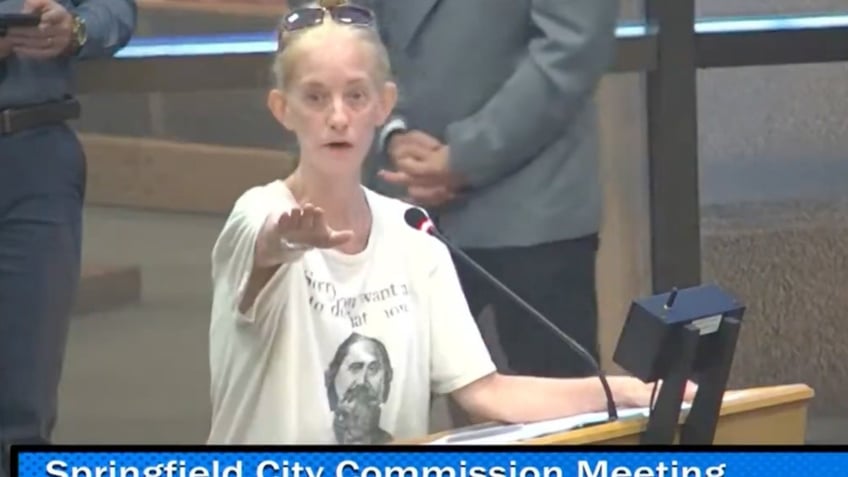 woman in white T-shirt at microphone at meeting