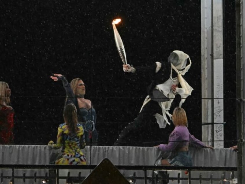 A torchbearer moves past models on a catwalk erected along the Passerelle Debilly bridge a