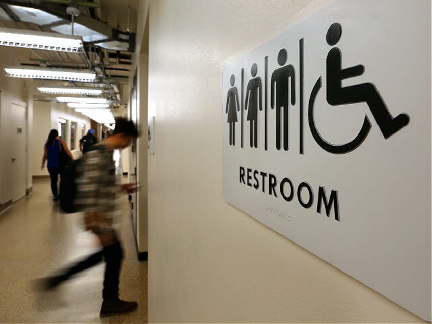 Students pass by a sign for a unisex bathroom next to the men's and women's restroom at th