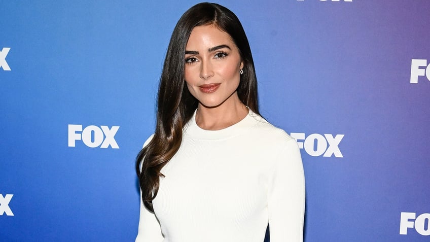 Olivia Culpo soft smiles in a white dress