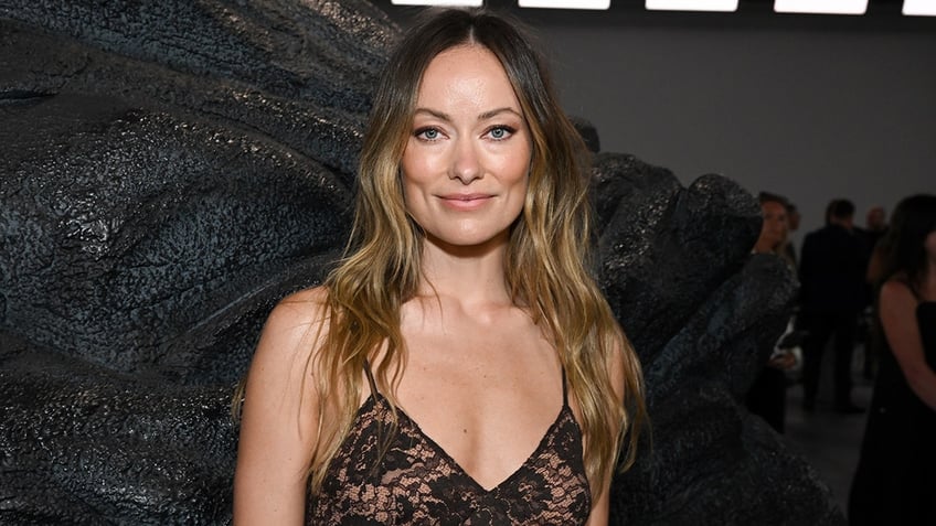 Olivia Wilde soft smiles in a black lacy v-neck dress