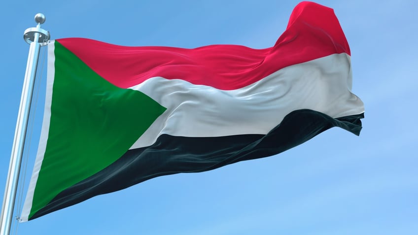 Palestinian flag flying atop a flagpole against a blue sky