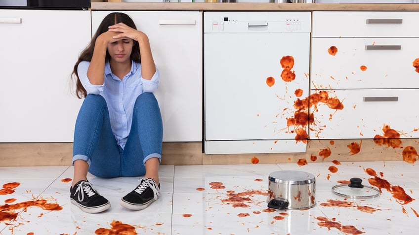 Unhappy Woman Sitting On Kitchen Floor With Spilled Food In Kitchen