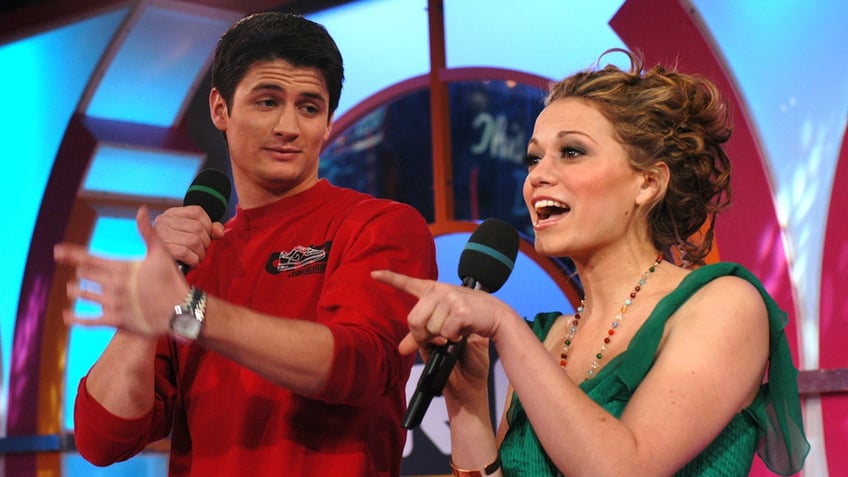 James Lafferty in a red shirt holding a microphone looks down at Bethany Joy Lenz in a green shirt holding a microphone