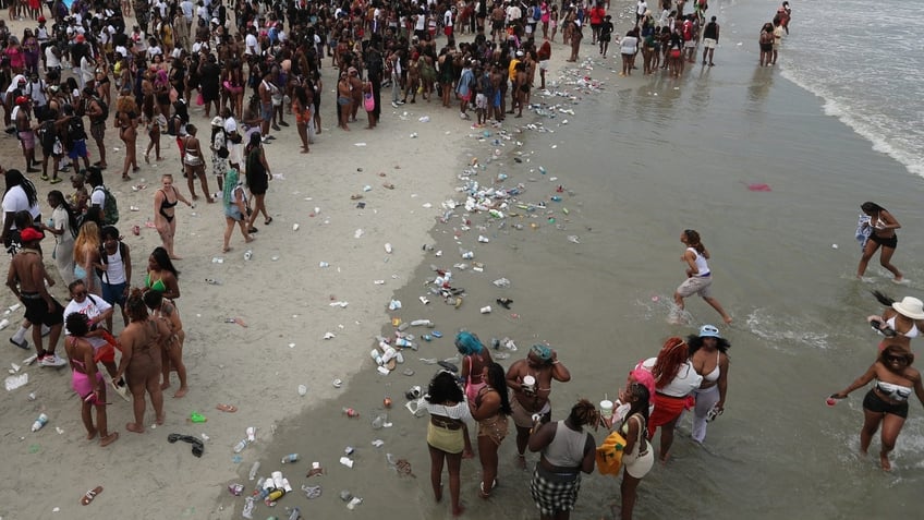 Trash can be seen along the beach as spring breakers party near the pier on Saturday, April 20, 2024 during Orange Crush on Tybee Island.