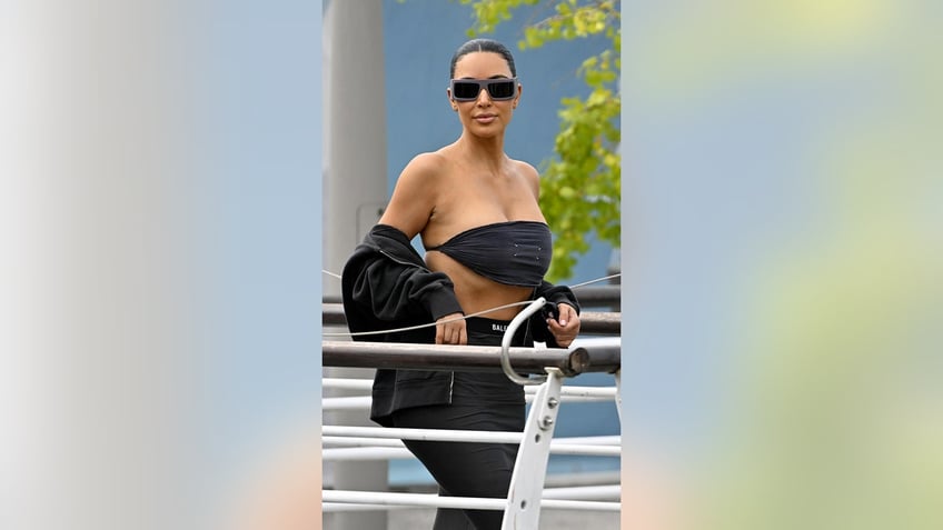 Kim Kardashian wearing a risque black crop top with a black skirt and a black jacket