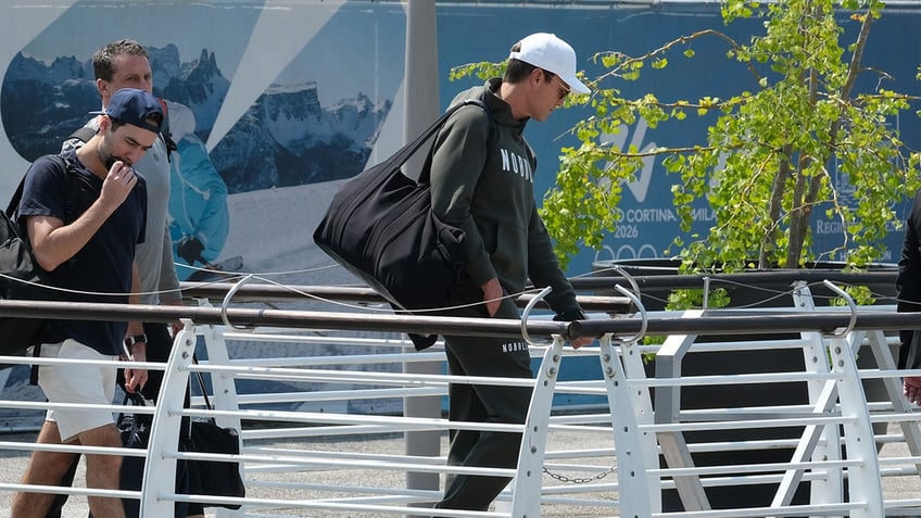 Tom Brady in a baseball cap and hoodie carrying a bag.
