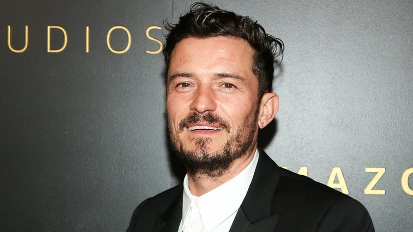 Orlando Bloom smiles in a white button down and black suit jacket on the red carpet