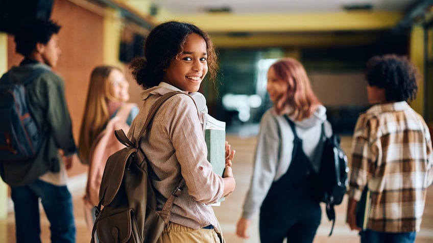 Happy high school student walking through hallway with her friends