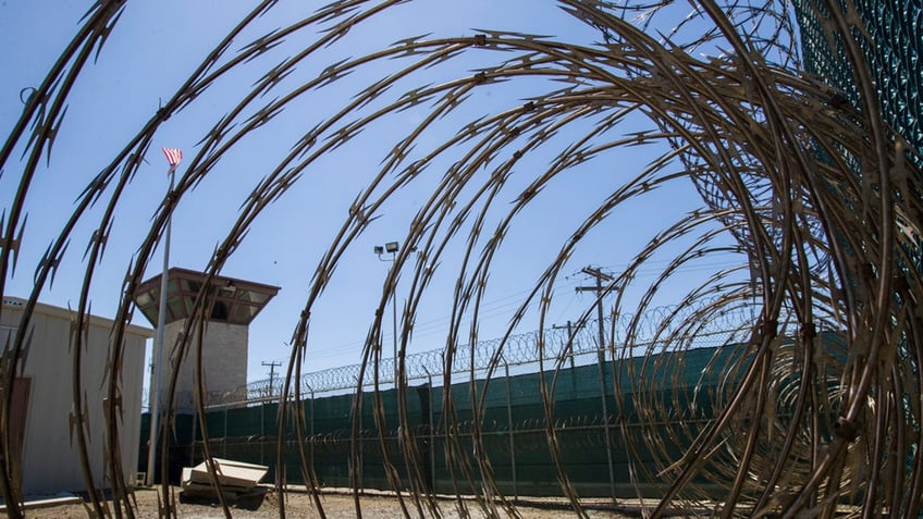 A control tower is seen through the razor wire inside a detention facility