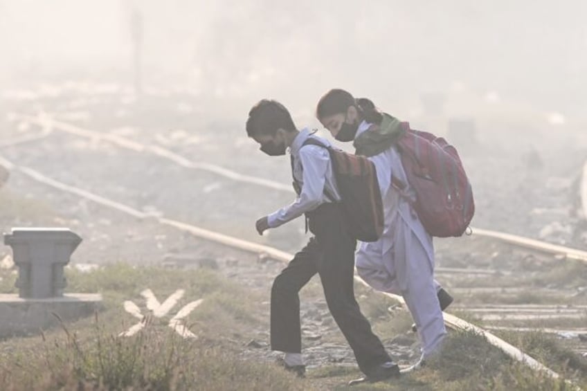 Schoolchildren wearing masks walk across a railway track amid thick smog in Lahore on Wedn