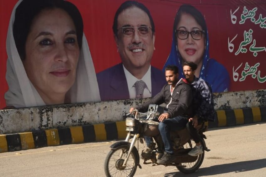 A motorcyclist and passenger ride past an election campaign poster of the Pakistan Peoples Party in Karachi ahead of the national vote on February 8