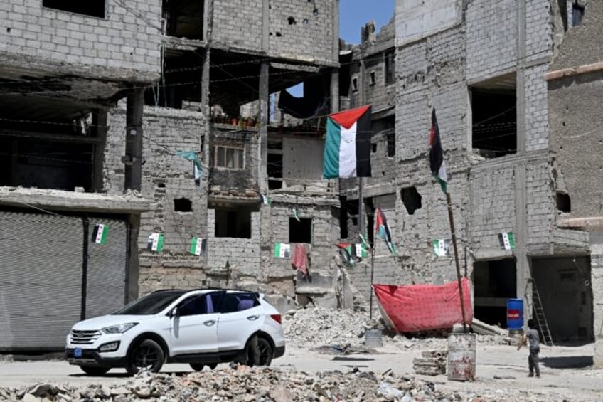 A boy walks under Palestinian and Syrian flags hanging outside buildings damaged during Sy