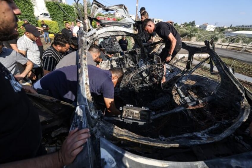 People near Tulkarem in the occupied West Bank check the remains of a car reportedly hit b