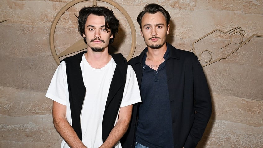 Dylan Lee in a white shirt and black thin vest and Brandon Lee in a black jacket and navy shirt on the carpet