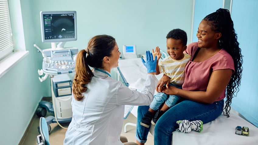 pediatrician high fives her young patient who's being held by his mother