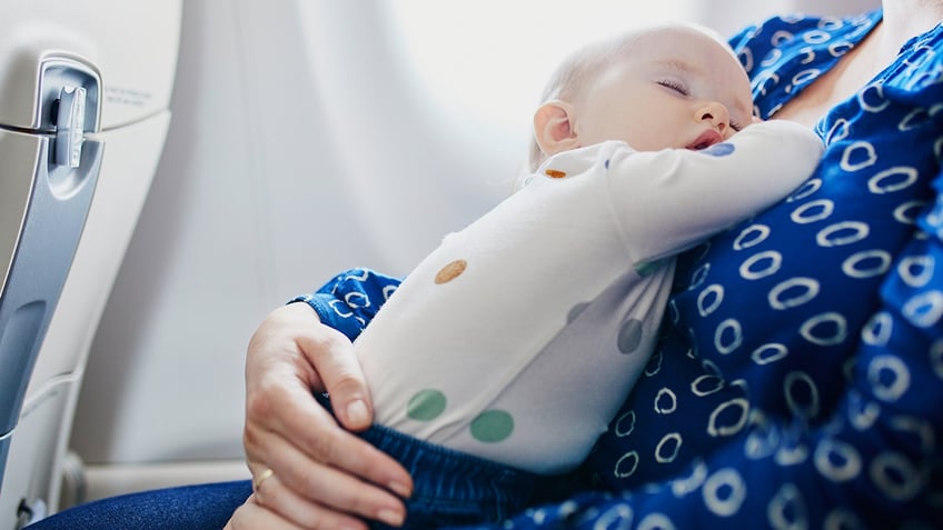 mother holding sleeping baby on flight