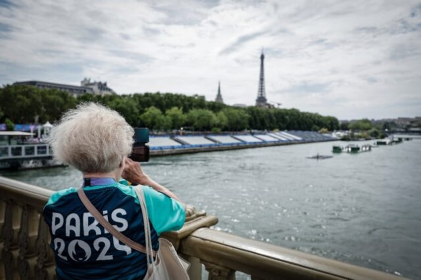 A Paris Olympics volunteer takes a picture of the stands lining the river Seine ahead of F