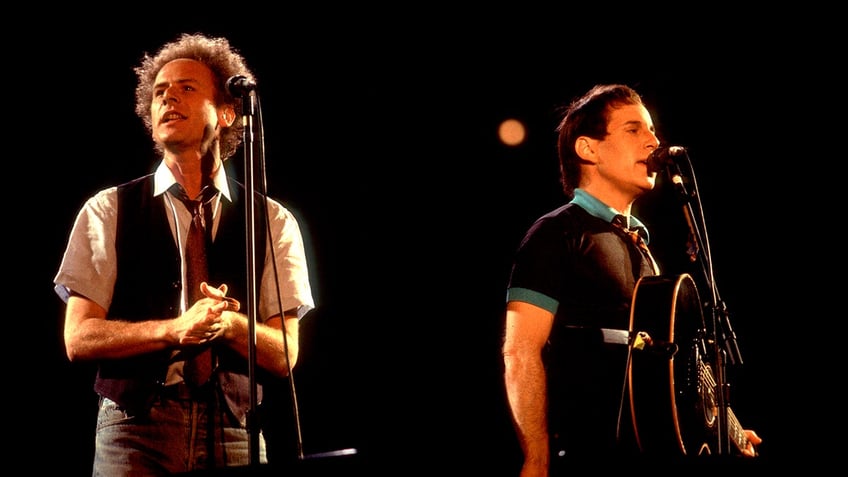 Art Garfunkel and Paul Simon singing into microphones but facing away from each other