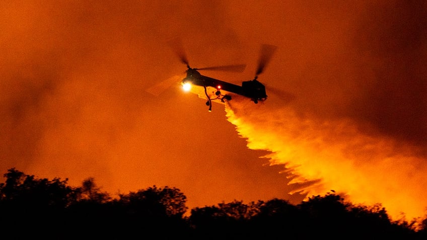 helicopter drops water on the Palisades Fire