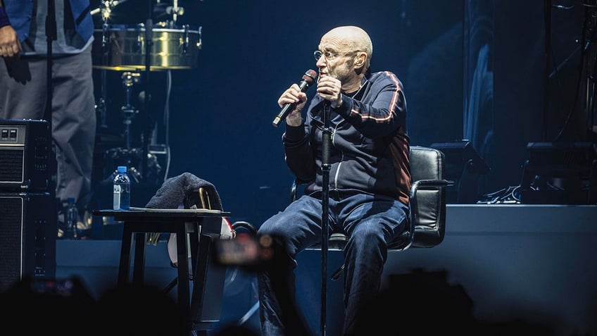 Phil Collins sitting in a chair while singing