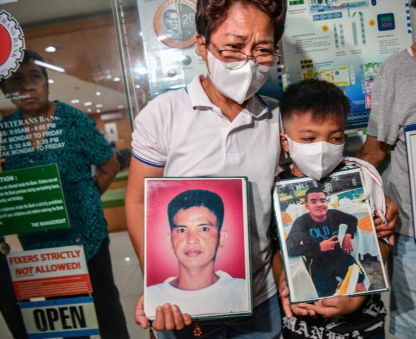 Mary Ann Domingo and her younger son hold portraits of her husband and son after four poli