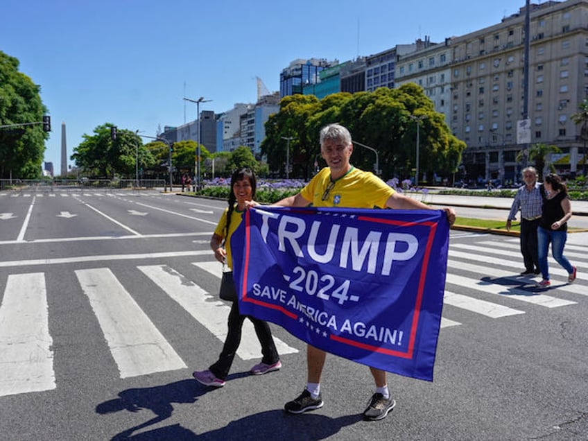 A couple wearing a Brazilian jersey and holding a flag of US' former President Donald Trump heads to the Congress to assist the inauguration ceremony of Argentina's President-elect Javier Milei, in Buenos Aires on December 10, 2023. Javier Milei will be sworn in as Argentina's president, as the country steels itself for harsh spending cuts and economic reforms aimed at curbing rampant inflation. (Photo by Gustavo ORTIZ / AFP)