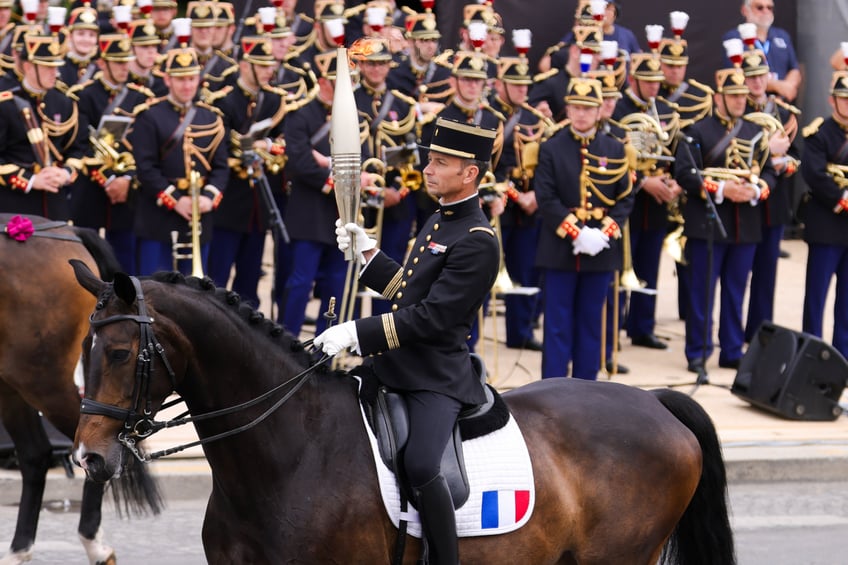 PARIS, FRANCE - JULY 14: Thibaut Valette is seen holding The Paris 2024 Olympic flame during the Bastille Day military parade as the Olympic Torch Relay arrives in Paris, on July 14, 2024 in Paris, France. The Olympic Flame arrived in Paris on July 14 to be integrated into the Bastille Day celebrations. This includes the traditional grand military parade on the Champs-Élysées, which is featuring the Olympic Torch as part of its route. The torch is planned to be carried through iconic locations in Paris, such as La Place de La Concorde, Notre Dame, Bataclan, Bastille, Assemblée Nationale, and the Musée Carnavalet. Additionally, the Eiffel Tower is hosting a special fireworks display, celebrating both Bastille Day and the upcoming Olympics with a theme centered around "Liberty." (Photo by Pierre Suu/Getty Images)