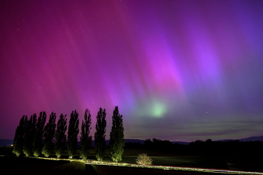 In this long exposure photograph, a car drives past and illuminates poplars as the northern lights glow in the night sky above the village of Daillens, Switzerland, early Saturday, May 11, 2024. (Laurent Gillieron/Keystone via AP)