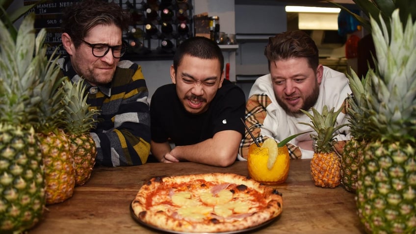 Francis Woolf, Quin Jianoran and Felix Rehberg, co-owners of Lupa Pizza in England, stare at a Hawaiian pizza and its pineapple topping.