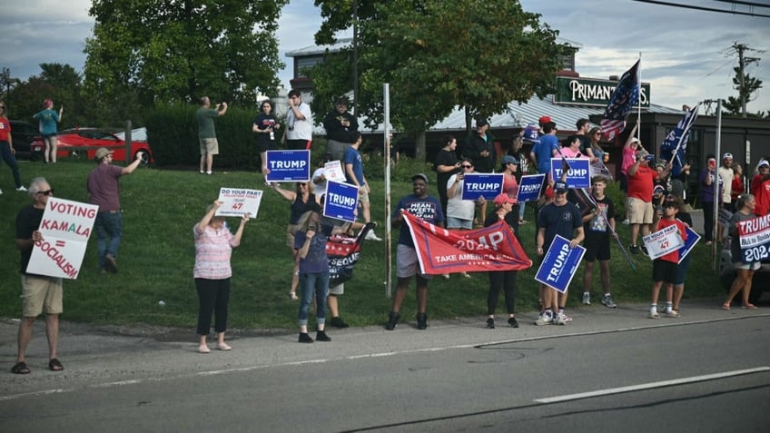 Supporters of former President and 2024 Republican presidential candidate Donald Trump hold signs and flags as Vice President and Democratic presidential candidate Kamala Harris makes a bus campaign tour stop at Primanti Bros. Restaurant and Bar in Moon Township, Pa., on Aug. 18, 2024.