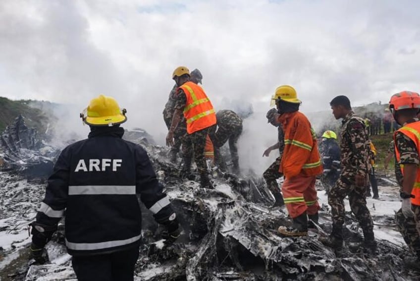 Rescuers and army personnel stand at the site after a Saurya Airlines' plane crashed durin