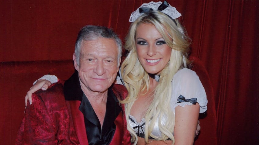 Crystal Hefner in a maids costume posing with Hugh Hefner in his red robe