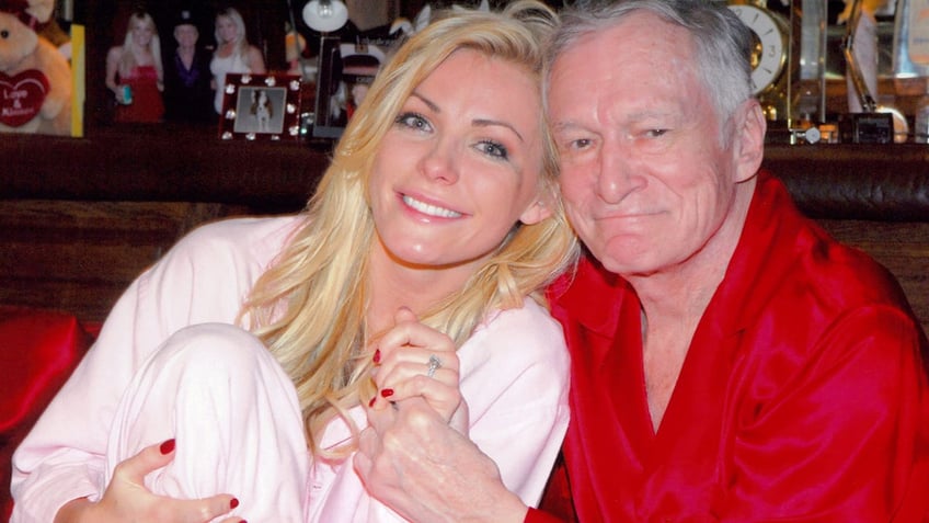 Crystal Hefner in pink pajamas showing off her engagement ring with Hugh Hefner who is wearing red pajamas