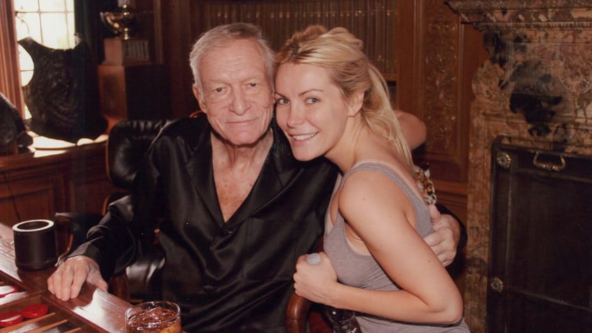 Crystal Hefner in a beige tank top leaning against Hugh Hefner