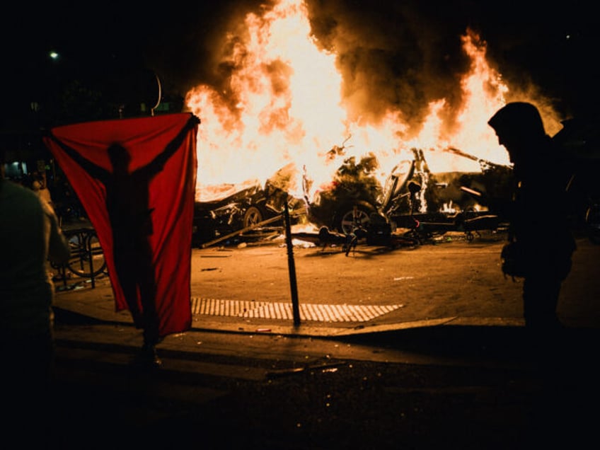 A person with a flag in front of two cars on fire during celebrations on the Place de la P