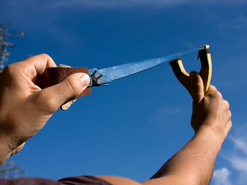 A rock is pulled back in an sling shot pointed to the sky - stock photo