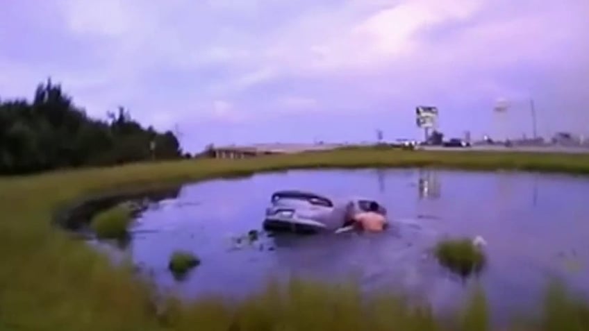 Car submerged in a lake with a man trying to open right door.